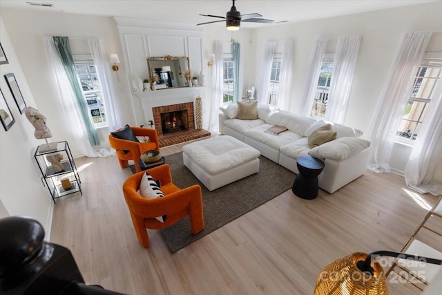 living area with a wealth of natural light, wood finished floors, a ceiling fan, and a brick fireplace