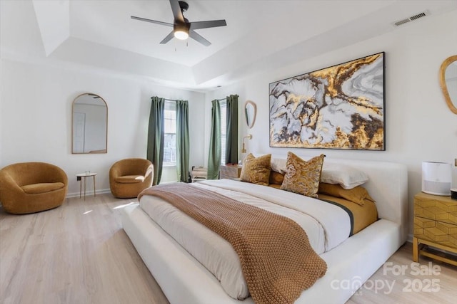 bedroom featuring visible vents, baseboards, ceiling fan, wood finished floors, and a tray ceiling