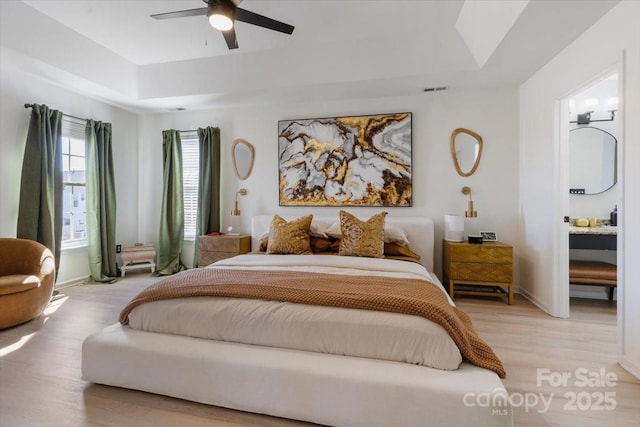 bedroom with a raised ceiling, baseboards, visible vents, light wood-style floors, and ceiling fan