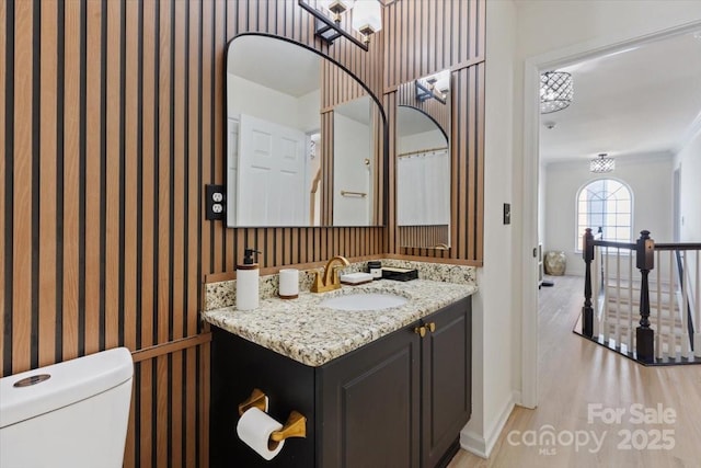 bathroom with toilet, vanity, wood finished floors, baseboards, and wallpapered walls