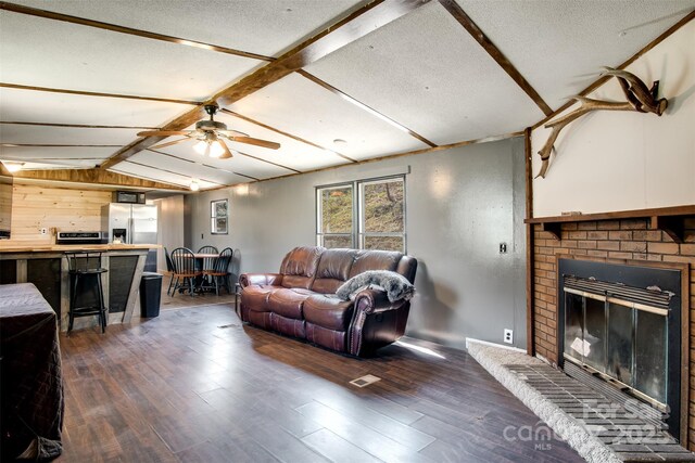 living room with a fireplace, vaulted ceiling with beams, wood finished floors, and ceiling fan