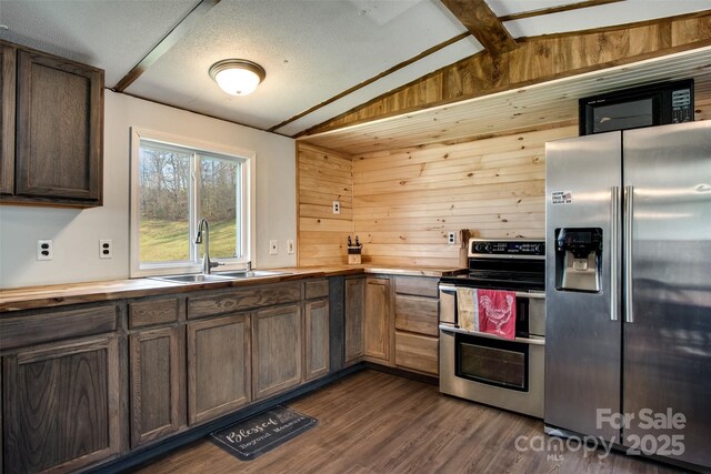 kitchen featuring wood walls, dark wood finished floors, appliances with stainless steel finishes, a sink, and vaulted ceiling