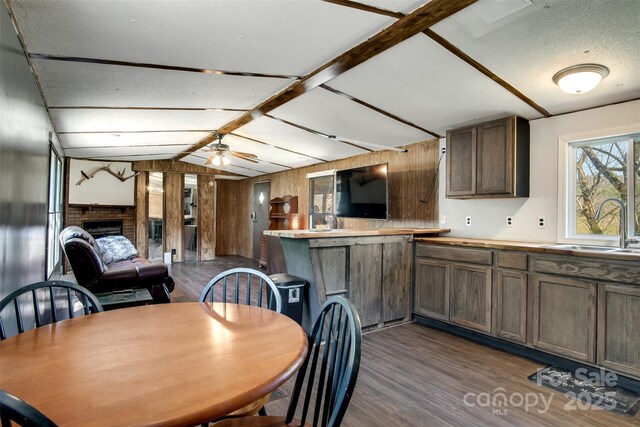 dining room featuring a brick fireplace, dark wood finished floors, wooden walls, a ceiling fan, and vaulted ceiling with beams