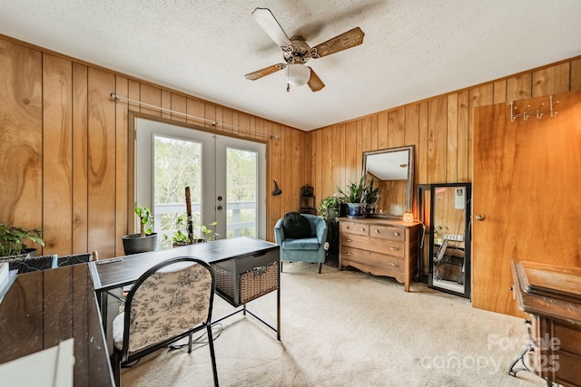 office space featuring light carpet, french doors, a textured ceiling, a ceiling fan, and wooden walls