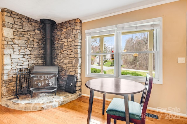 dining space featuring baseboards, wood finished floors, a wood stove, and a healthy amount of sunlight