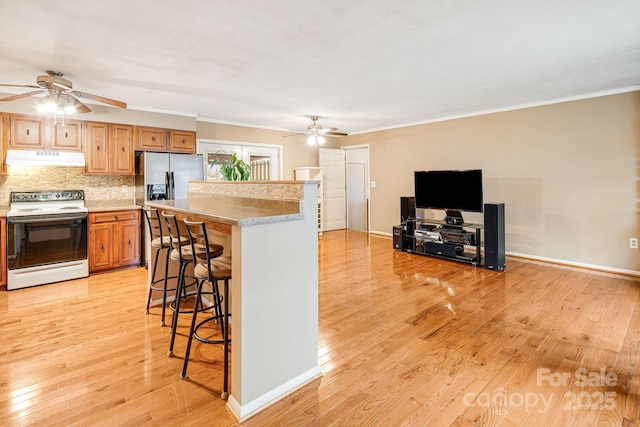 kitchen featuring white range with electric cooktop, a ceiling fan, under cabinet range hood, and light wood finished floors