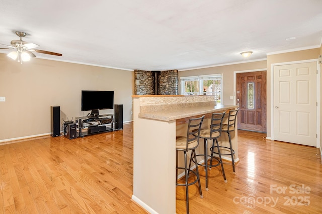 kitchen with light wood finished floors, crown molding, a kitchen breakfast bar, and a ceiling fan