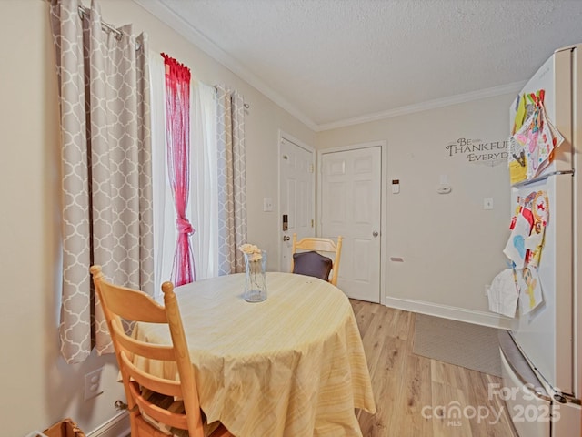 dining room with light wood-type flooring, ornamental molding, a textured ceiling, and baseboards