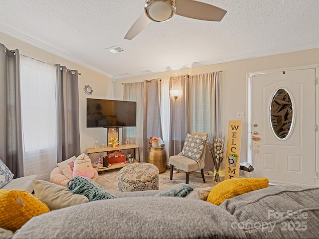 living area with a textured ceiling, ornamental molding, and a ceiling fan