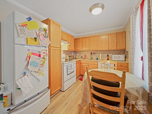 kitchen with white appliances, under cabinet range hood, crown molding, light wood finished floors, and a sink