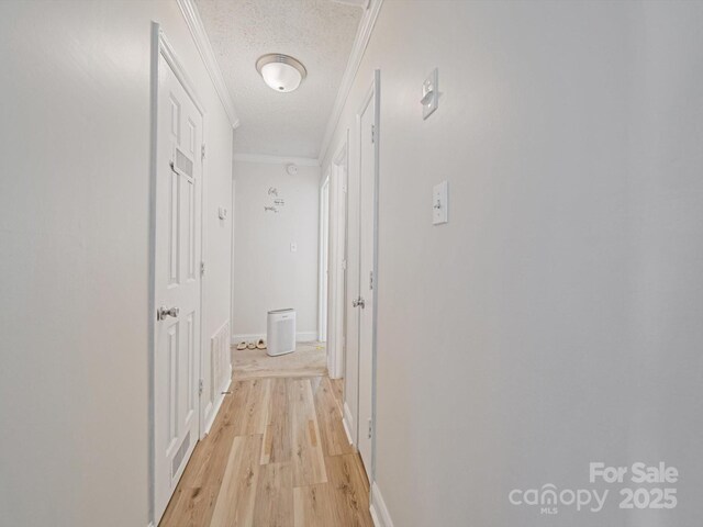 corridor with light wood finished floors, a textured ceiling, and ornamental molding