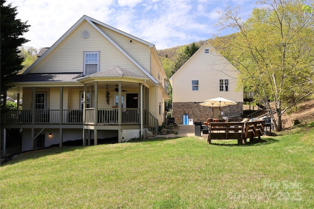 back of property featuring a yard, covered porch, a ceiling fan, and a shingled roof