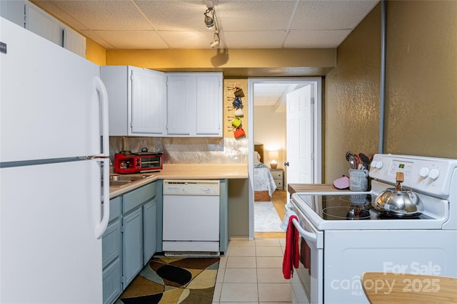 kitchen featuring white appliances, light countertops, rail lighting, blue cabinets, and a paneled ceiling