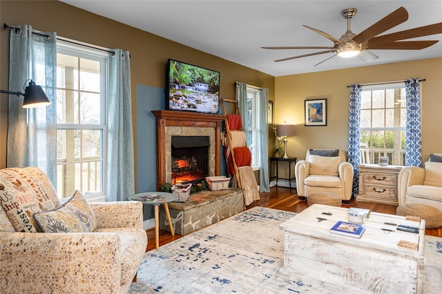 living area featuring ceiling fan, wood finished floors, and a stone fireplace