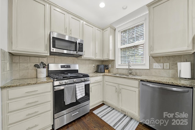 kitchen featuring dark wood-style flooring, stainless steel appliances, decorative backsplash, a sink, and light stone counters