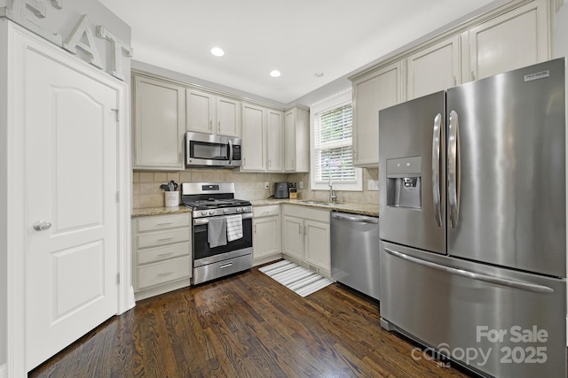 kitchen featuring decorative backsplash, a sink, dark wood-style floors, light stone countertops, and appliances with stainless steel finishes