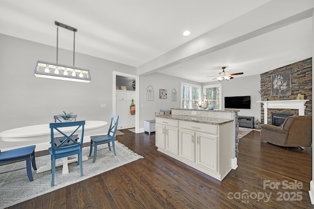 kitchen with open floor plan, decorative light fixtures, dark wood finished floors, a ceiling fan, and a fireplace