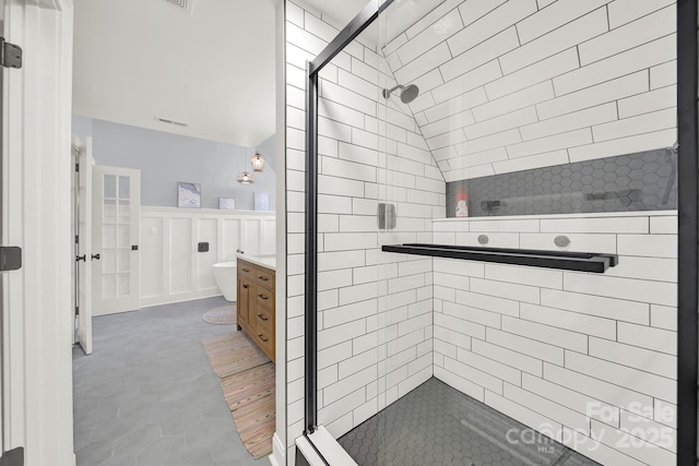 full bath featuring a stall shower, vanity, wainscoting, lofted ceiling, and a decorative wall