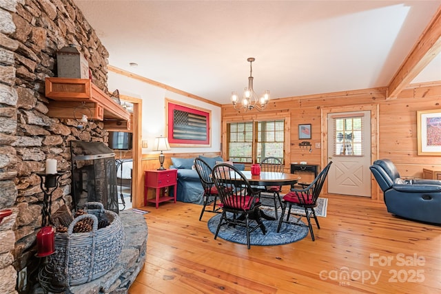 dining space with light wood-type flooring, an inviting chandelier, a fireplace, and wooden walls