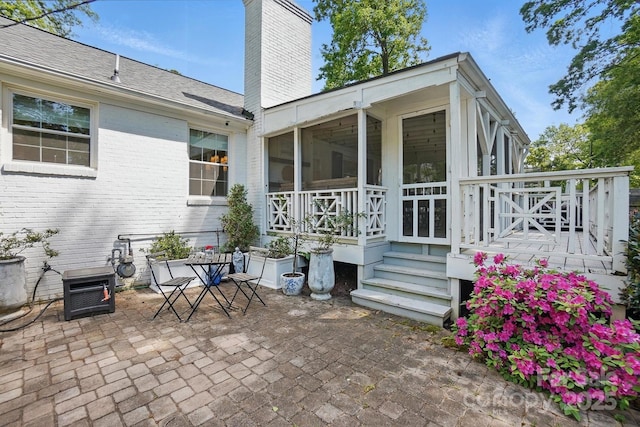 back of house featuring brick siding, a wooden deck, a sunroom, a chimney, and a patio