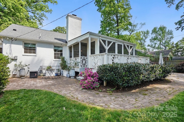 rear view of property with a patio, a chimney, a sunroom, a shingled roof, and brick siding
