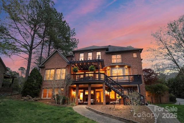 back of property at dusk with a lawn, fence, stairway, brick siding, and a wooden deck