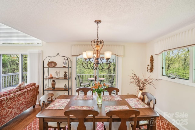 dining space featuring wood finished floors, an inviting chandelier, and a textured ceiling