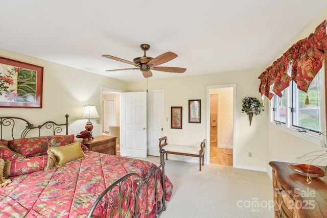 bedroom featuring ceiling fan, ensuite bath, baseboards, and light colored carpet