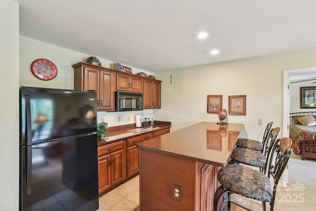 kitchen with black appliances, brown cabinets, a kitchen bar, a peninsula, and recessed lighting
