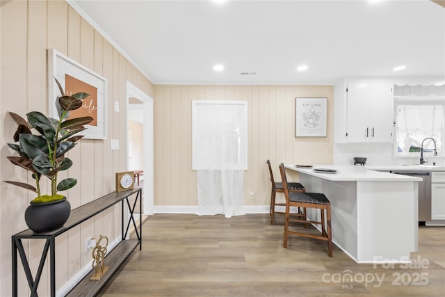 kitchen featuring light wood-style floors, stainless steel dishwasher, white cabinetry, a breakfast bar, and light countertops