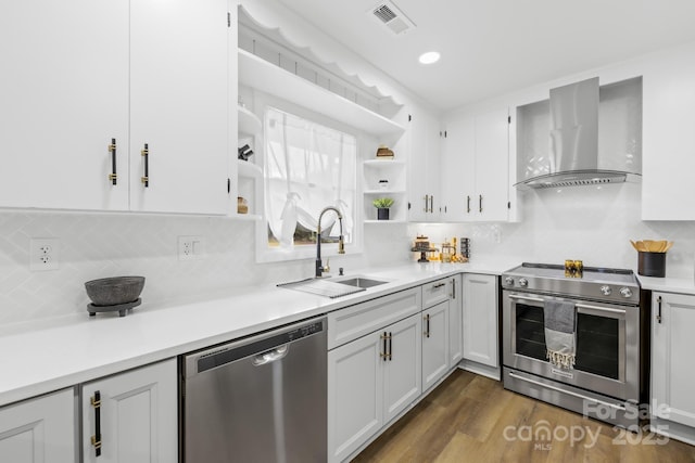 kitchen featuring wall chimney range hood, open shelves, visible vents, a sink, and stainless steel appliances
