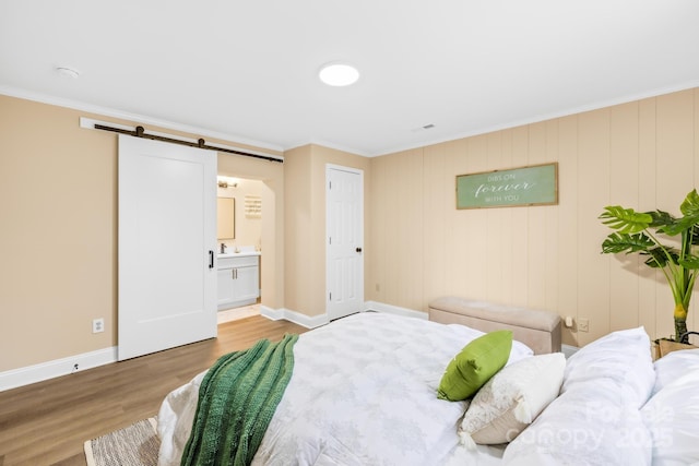 bedroom featuring baseboards, crown molding, connected bathroom, a barn door, and wood finished floors