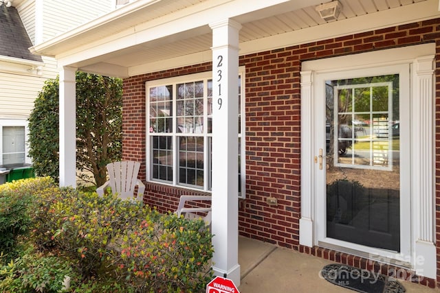 entrance to property featuring covered porch and brick siding