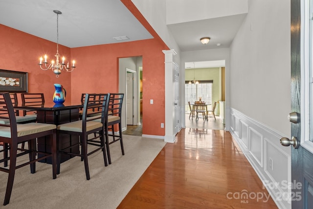 dining space featuring visible vents, a decorative wall, wood finished floors, and a chandelier