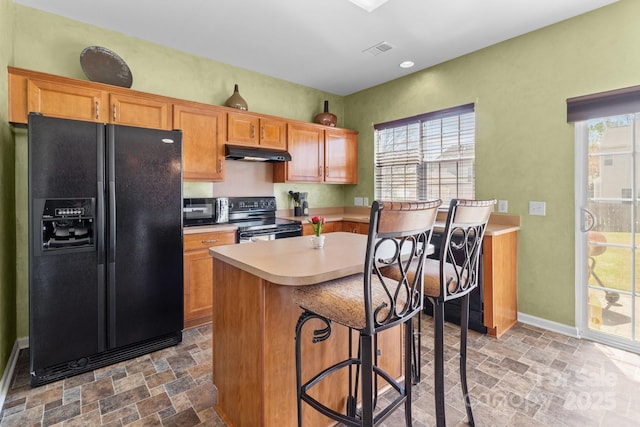 kitchen with light countertops, stone finish flooring, under cabinet range hood, visible vents, and black appliances