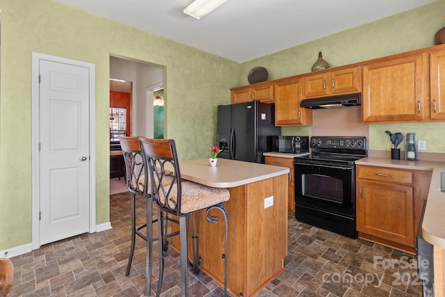kitchen featuring light countertops, a center island, under cabinet range hood, stone finish flooring, and black appliances