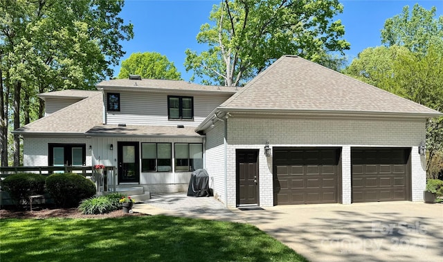 rear view of property with a garage, driveway, a shingled roof, and brick siding