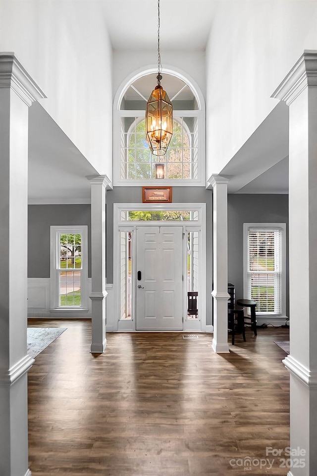 1214 Foxfield Rd, Waxhaw, NC 28173 - entryway featuring decorative columns, a high ceiling, wood finished floors, a chandelier, and wainscoting