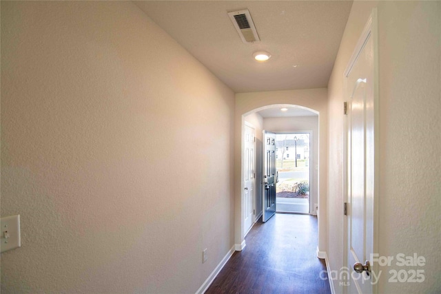 hallway featuring arched walkways, baseboards, dark wood-style floors, and visible vents