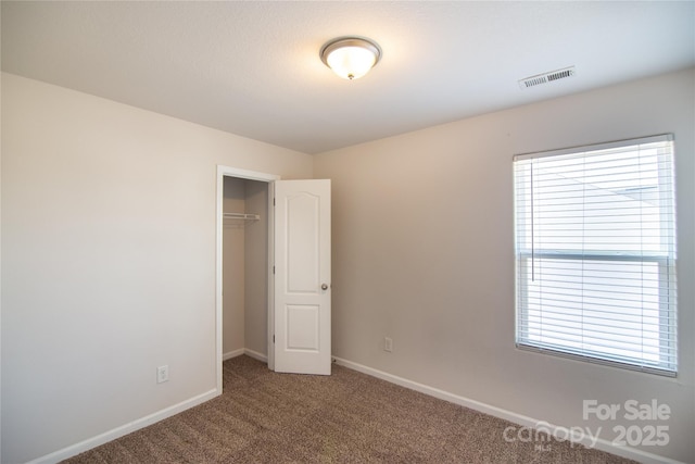 unfurnished bedroom with a closet, carpet flooring, visible vents, baseboards, and a walk in closet