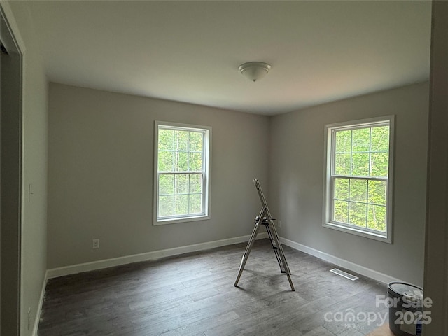unfurnished room featuring healthy amount of natural light, wood finished floors, and baseboards