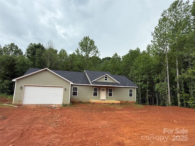 view of front of property with driveway, an attached garage, a shingled roof, and a wooded view