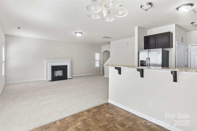 kitchen with stainless steel refrigerator with ice dispenser, a chandelier, a breakfast bar, visible vents, and light carpet