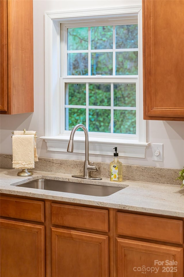 kitchen with brown cabinetry, light stone countertops, and a sink