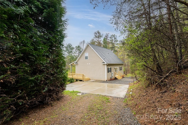 view of home's exterior featuring driveway, roof with shingles, and a deck