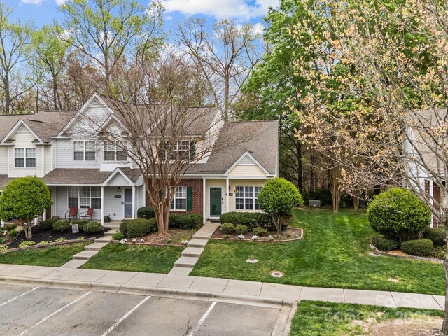 view of front of property with covered porch, uncovered parking, roof with shingles, and a front yard