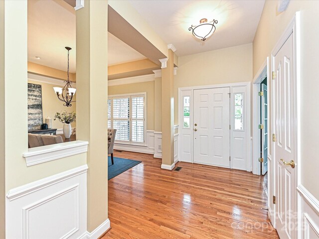 entrance foyer featuring light wood-style floors, a wainscoted wall, a chandelier, decorative columns, and a decorative wall