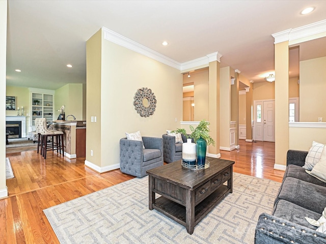 living area featuring crown molding, light wood-style floors, recessed lighting, baseboards, and a glass covered fireplace