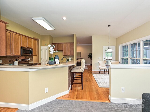 kitchen featuring stainless steel appliances, brown cabinets, light wood finished floors, backsplash, and recessed lighting