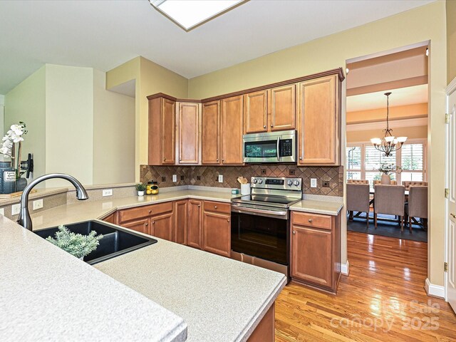 kitchen with appliances with stainless steel finishes, a sink, light countertops, light wood-style floors, and tasteful backsplash